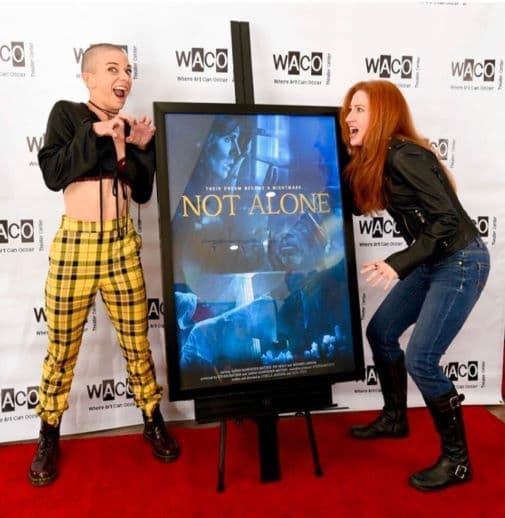 Andi Norris and Bekka Prewitt standing on a red carpet with a movie poster for Not Alone.