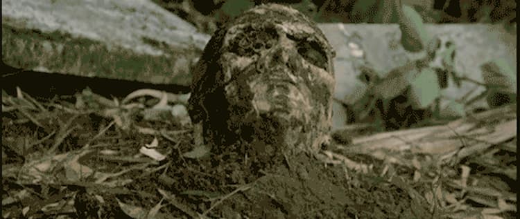 Zombie head emerging from the ground in the film Zombie