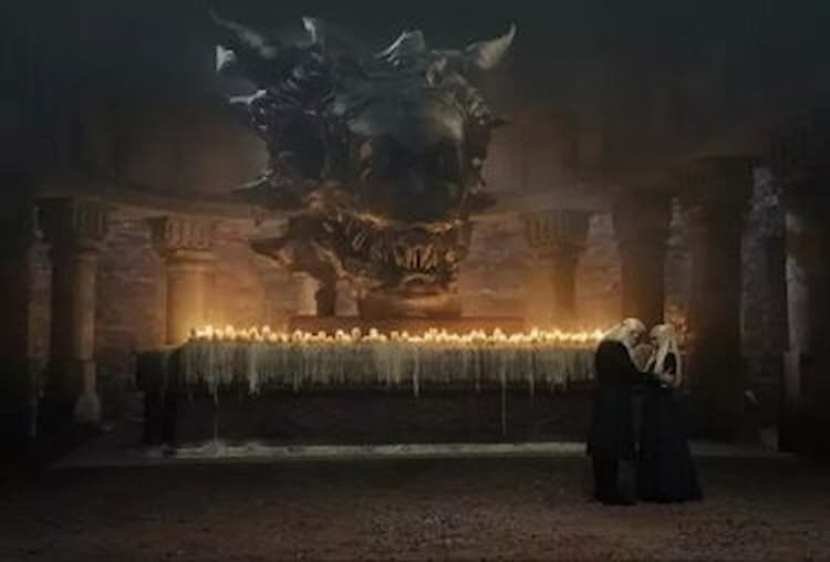 Balerion the Black Dread’s skull sits atop a shrine of lit candles as King Viserys and Princess Rhaenyra have a deep discussion in front of it.
