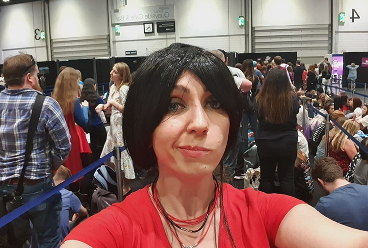 A selfie of Lily K in her cosplay of Chloe Frazer from Uncharted with a long, crowded line of people behind her, spiraling through stanchions.