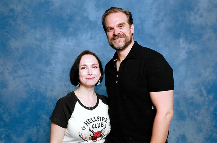 Lily K in a posted photo with David Harbour, both smiling, with a blue backdrop.
