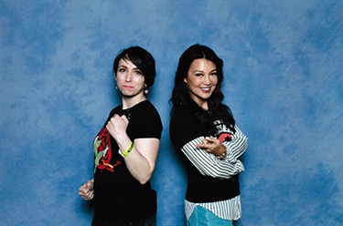 Lily K in a posed photo with actor Ming Na Wen, standing back-to-back, with a blue backdrop.