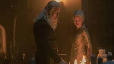 King Viserys and Rhaenyra are in a dimly lit chamber looking into the fire in a brazier. Viserys is reaching for a dagger that's sitting in the fire.