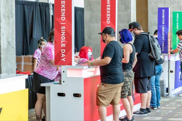 Photo taken from a booth of two RTX volunteers, called Guardians, sitting down and one standing up behind a booth checking in RTX attendees in front of it.