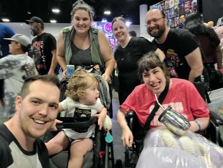 Photo on the convention floor of Jake Brown and his wife with their daughter in a stroller, standing next to Shana Martin in her wheelchair with Maria and Jake Kinnun behind her. 
