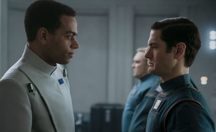 An Imperial officer has a slight smile while facing Syril Karn, who is standing at attention but glancing downward as if guilt-ridden.