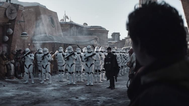 A group of Republic-era clone troopers turns around and readies their blasters whilst an officer in black commands them.