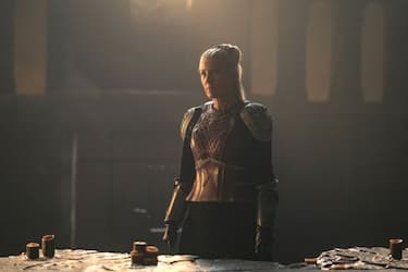 Rhaenys stands at the dark war table in her dragon-riding armor, detailed with gold shoulder caps and red scales.