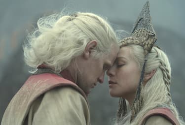 Daemon and Rhaenyra embrace each other during their private wedding, wearing traditional Valyrian clothing of red and white.