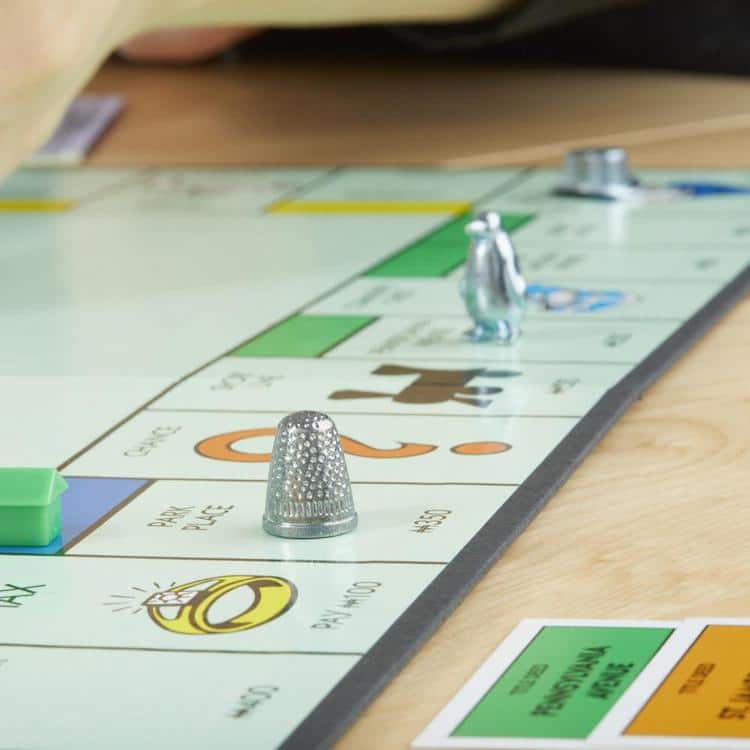 Top hat, penguin, and thimble game pieces played on a Monopoly board