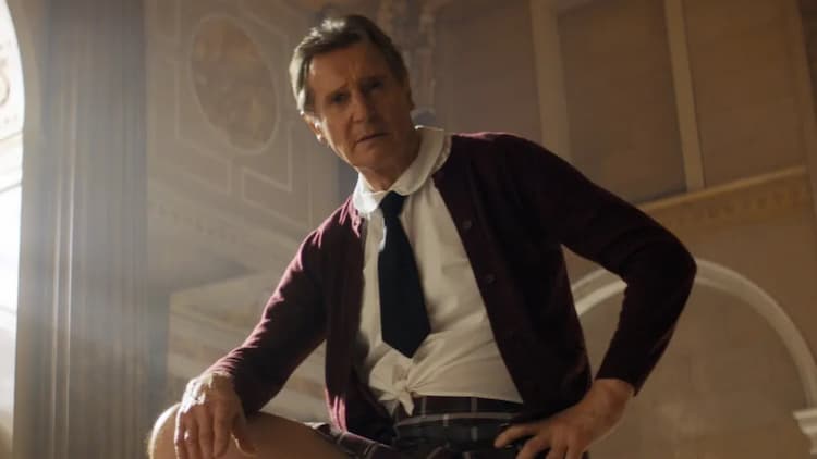 Frank is in a bank. He is resting his right hand on his leg. He is wearing a disguise. The disguise is a little girl's outfit.